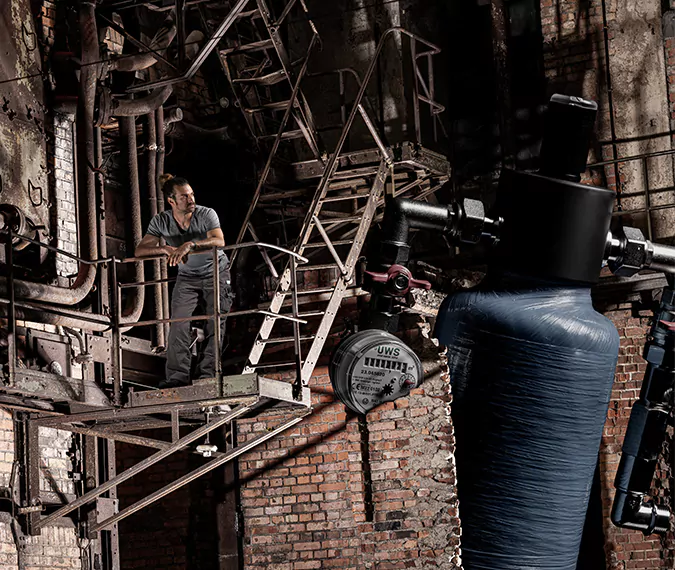 ein Mann lehnt am Geländer in einer Industriehalle, im Hintergrund ein UWS Gerät zu sehen