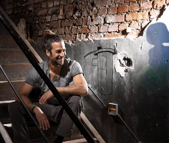 ein Mann, daneben MAGella als Graffiti auf der Wand